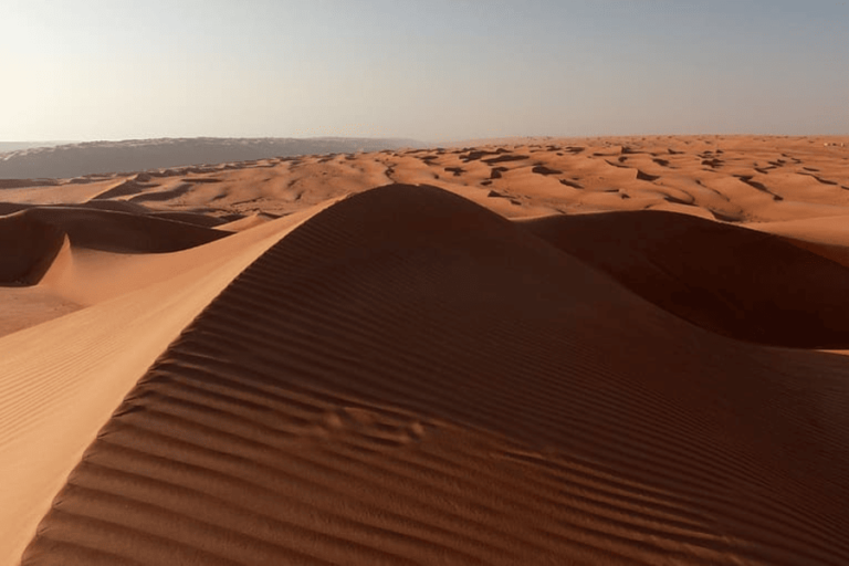 Visite Oman : traversée de la route désert avec une vue sur un paysage désertique orangé apaisant.