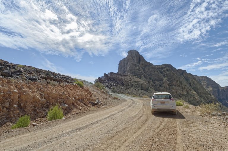 Trekking Oman : une voiture blanche sur une route avec une vue sur un paysage désertique orangé apaisant lors de cette traversée.