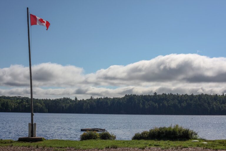 Voyage au Canada : un drapeau au bord d'un lac bordé d'une forêt Akaoka