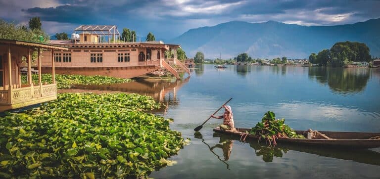 Voyage en Inde : une femme sur une pirogue avec des légumes en face des montagnes Akaoka