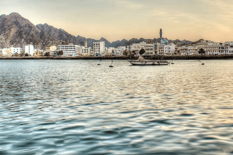 Mer d'Oman, située au bord d'une ville avec des bâtisses blanche et à l'arrière dans le paysage de forêt.