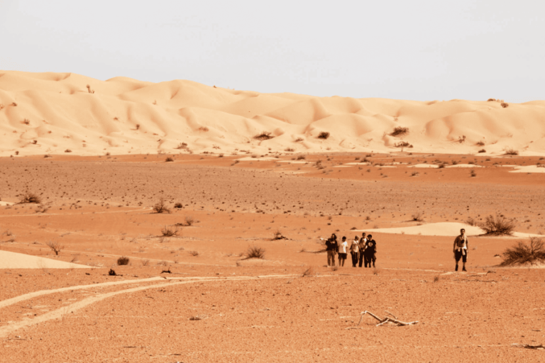 Désert Oman, des randonneurs marchent sur le sable orangé du désert admirant un paysage apaisant.