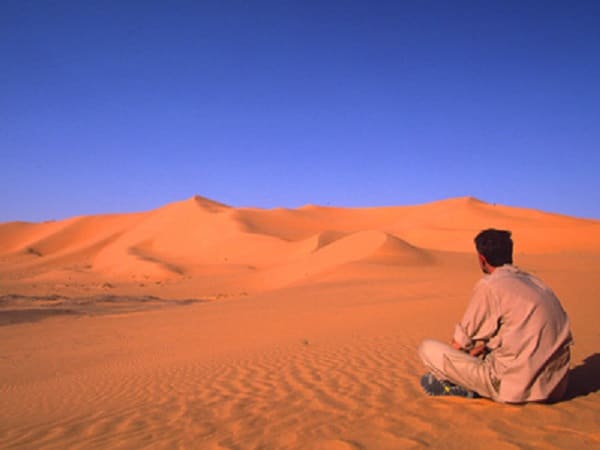 Voyage en Algérie : touriste assis sur le sable de l'Erg Chech dans le Sud-Ouest Akaoka