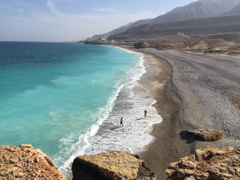 Excursions Oman : Des touristes sur la plage avec des montagnes en hauteur admirant le paysage.