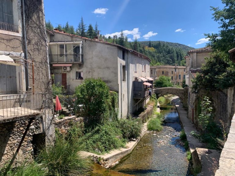 Randonnée Cévennes : Ruisseau passant au milieu des maisons et des collines à l'horizon